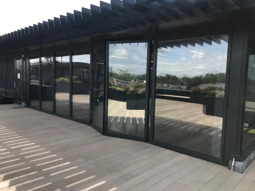Dark-grey aluminium bifold doors folded open onto a rooftop terrace beneath an overhead blade canopy, Hammersmith